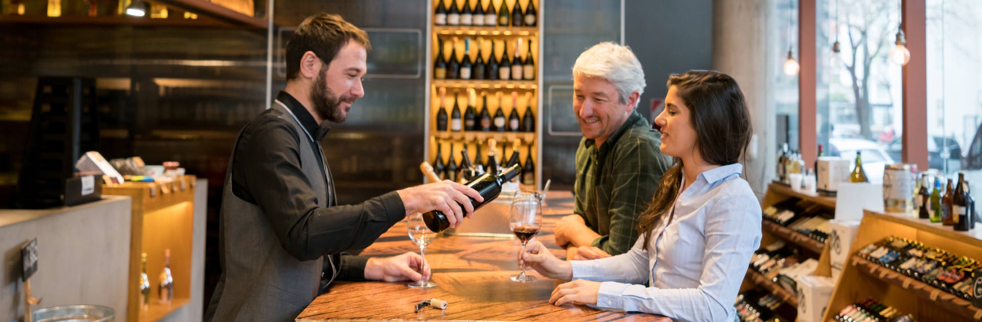 Wine tasting room shop keeper pouring wine for man and woman.