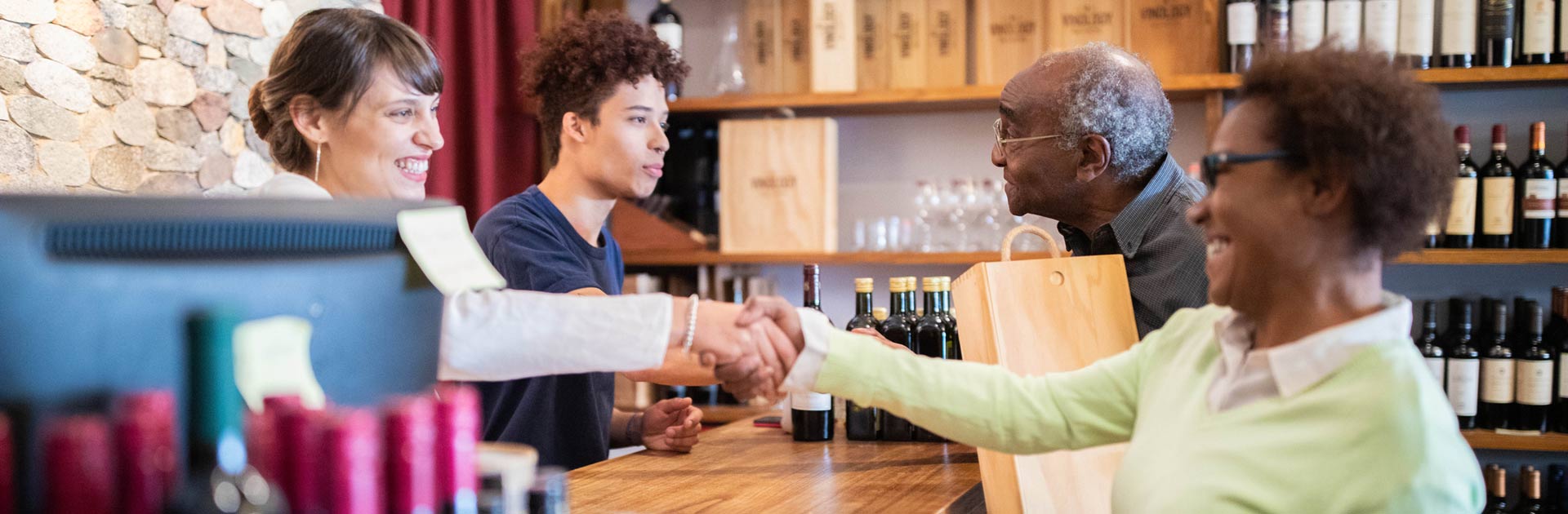Retail wine shop with customer shaking hand with cashier.