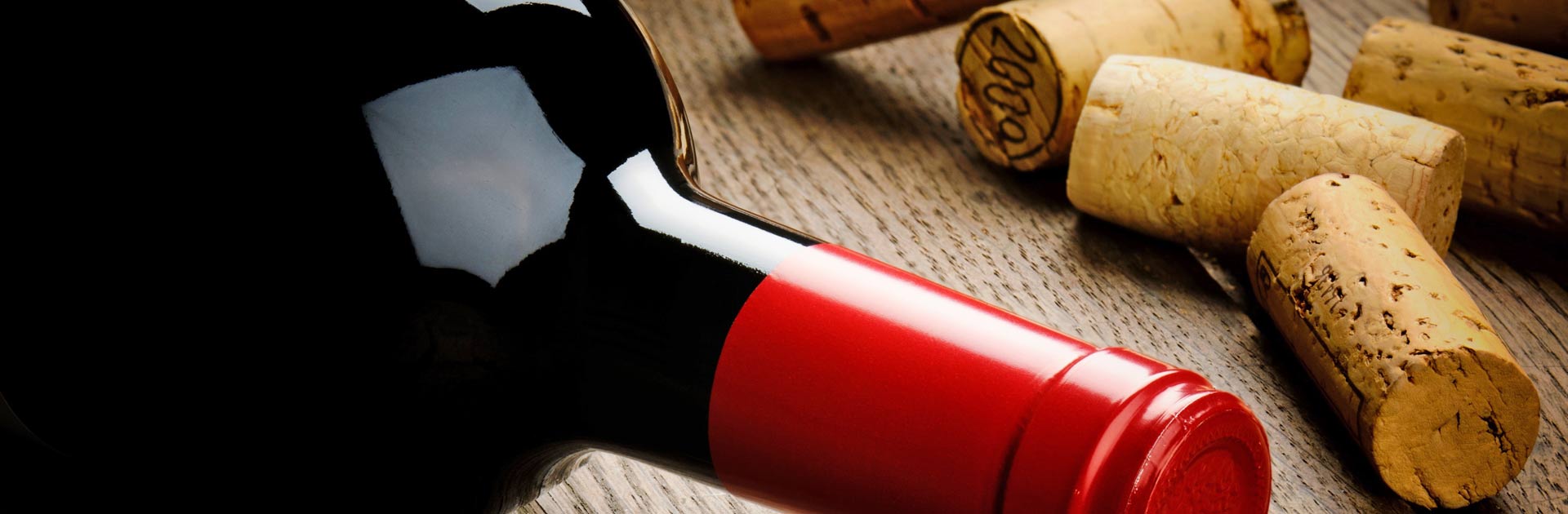 Close up of a wine bottle with dark red wine, posed with wine corks.